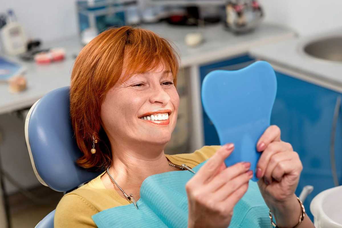 Patient viewing her smile in a mirror after dental treatment